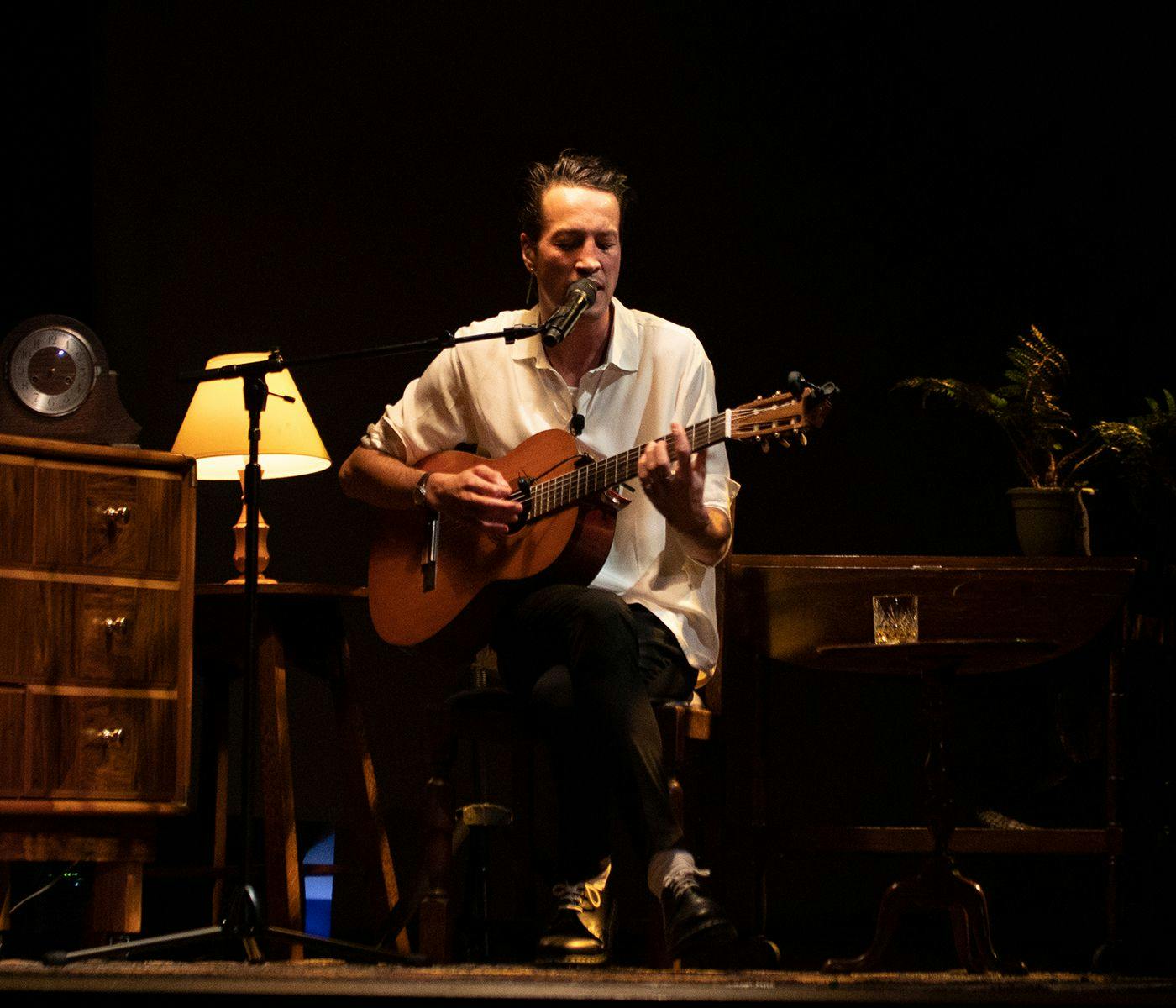 Marlon Williams seated, playing the guitar.