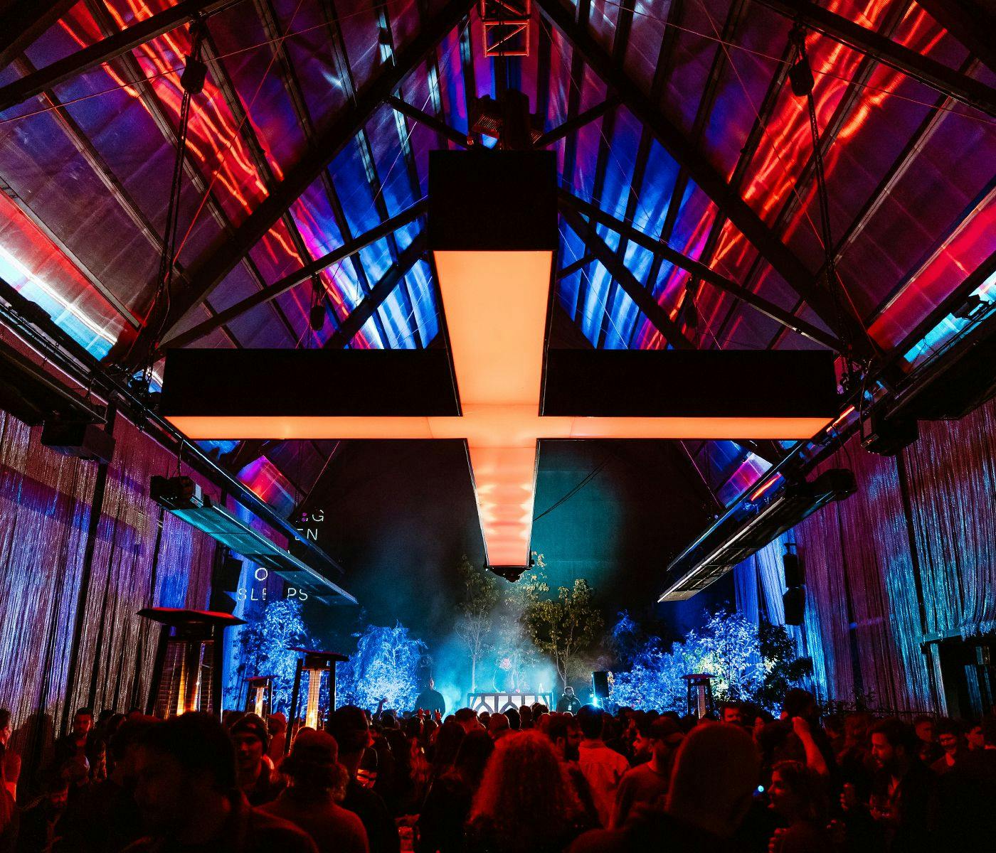 In The Hanging Garden at night, a giant red cross hangs from the roof of Cathedral with a crowd underneath.