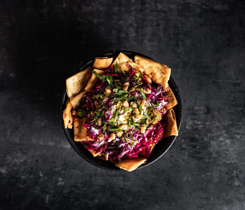 A bowl of middle eastern nachos, packed with hummus, tahini, cabbage and nuts.