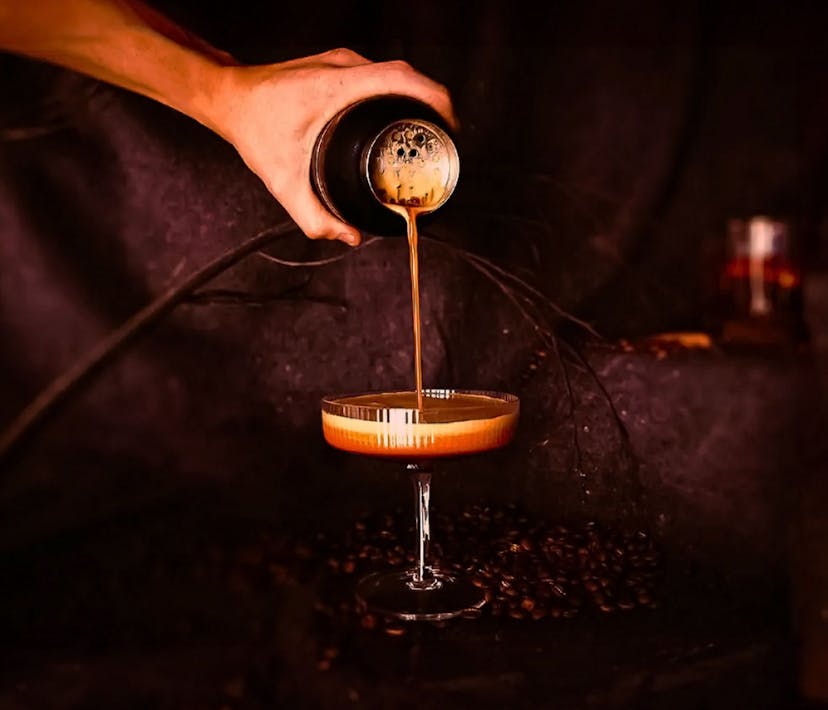 An espresso martini being poured into a large cocktail glass.