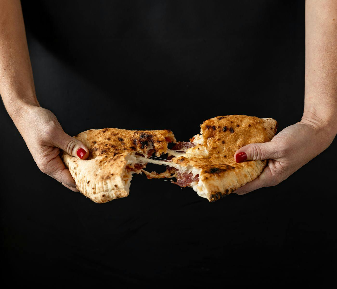 A calzone being pulled apart, oozing pepperoni and melted cheese.