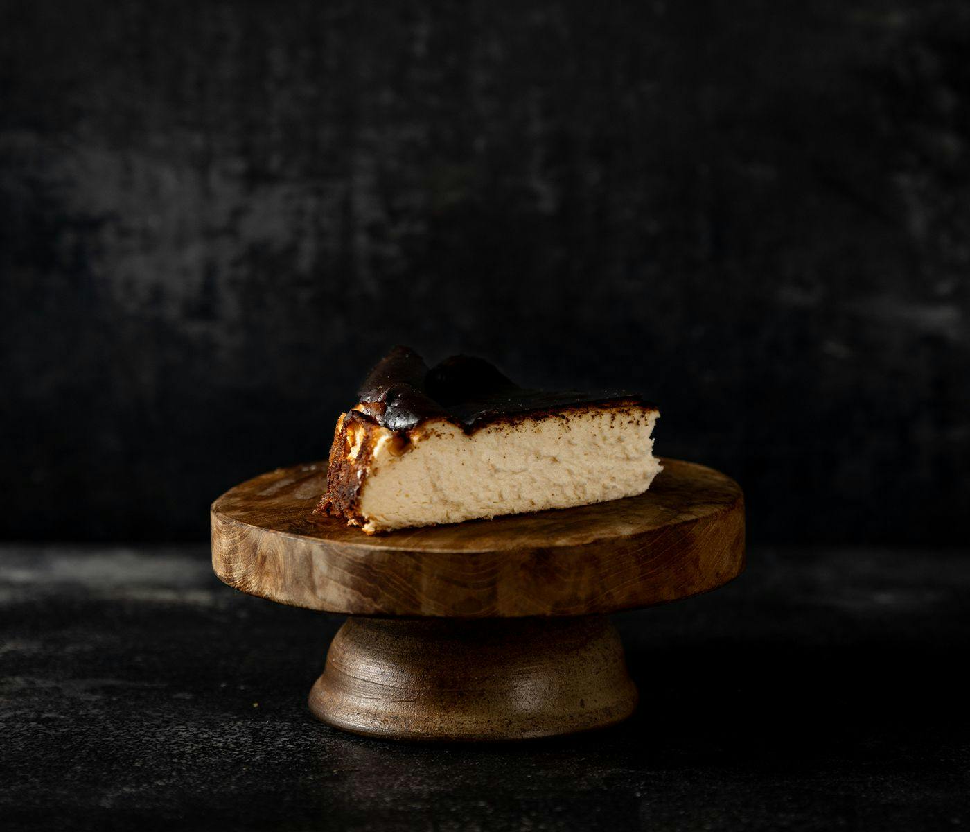 A slice of Basque Cheesecake sitting on a wooden pedestal.