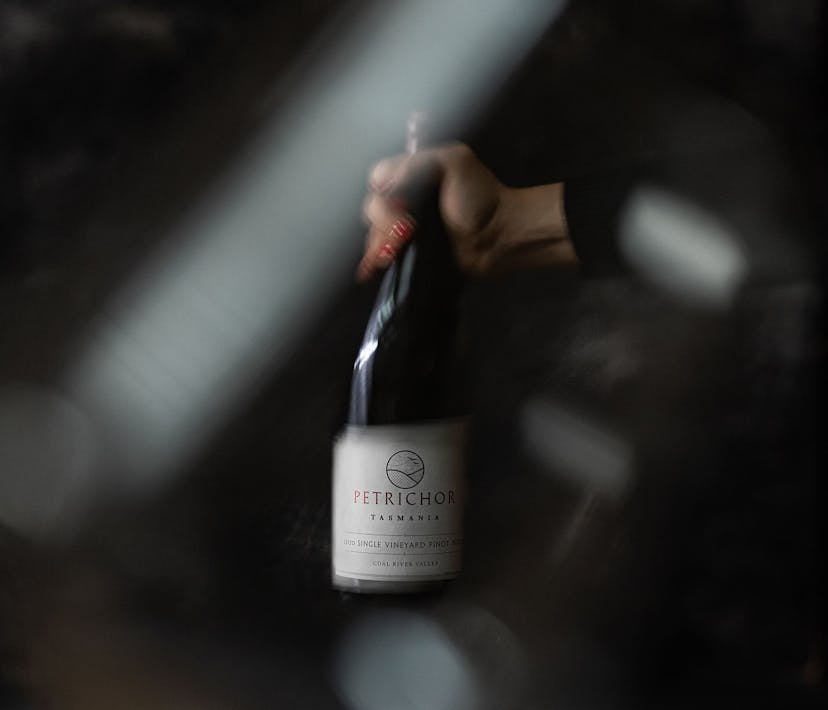 A blurry image of a hand holding a bottle of Petrichor wine.