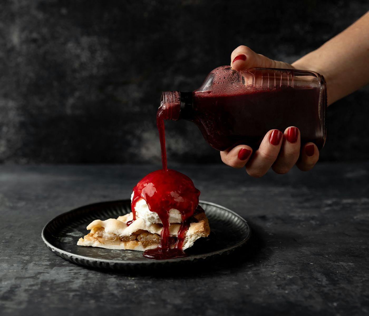 Red raspberry coulis is poured over ice cream and apple pie.