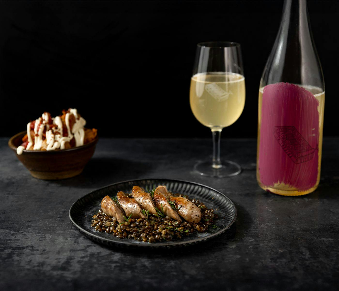 A plate of Spanish sausage and lentils, with a glass and bottle of white wine.