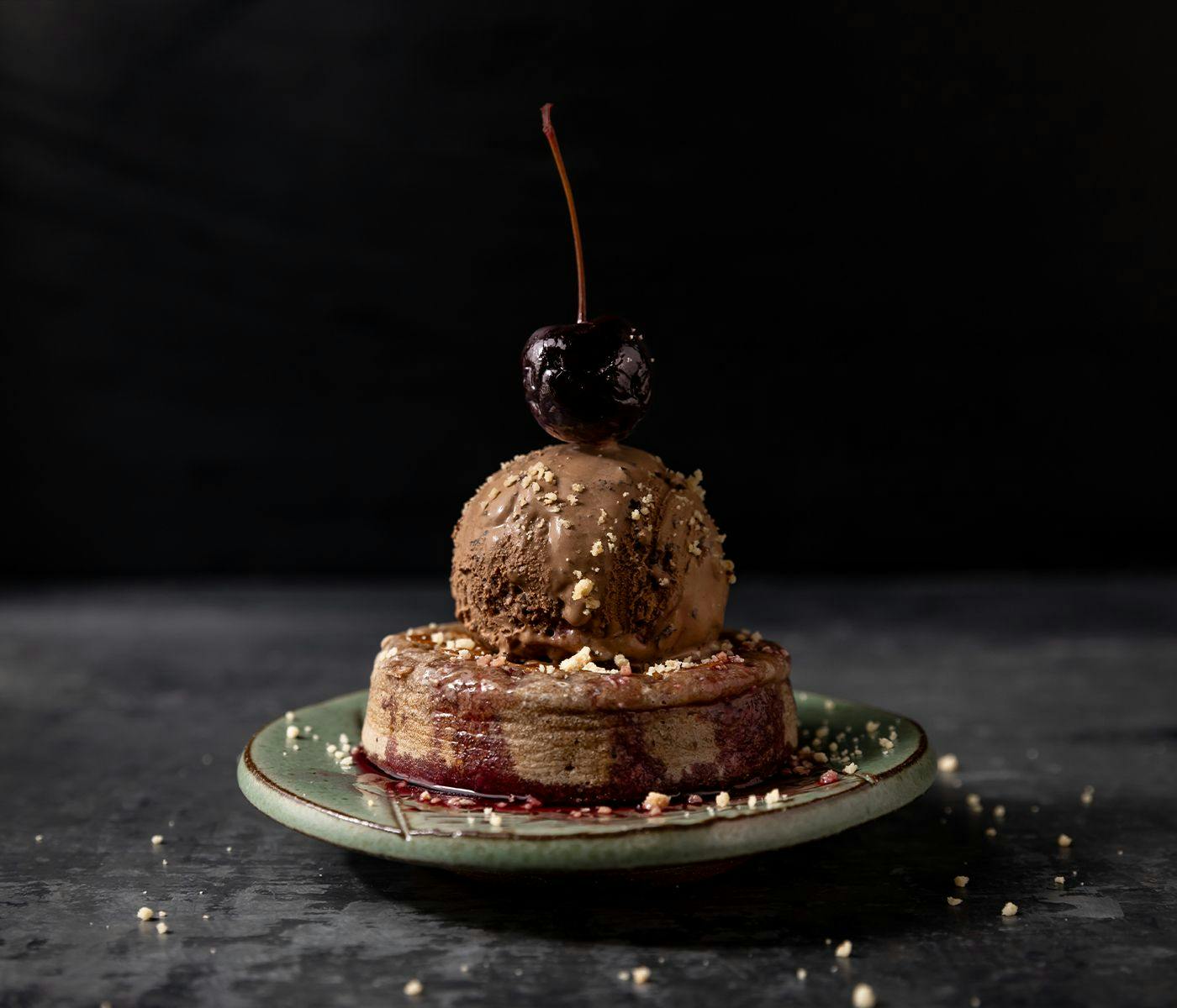 A crumpet topped with chocolate ice cream, and a dark red cherry.