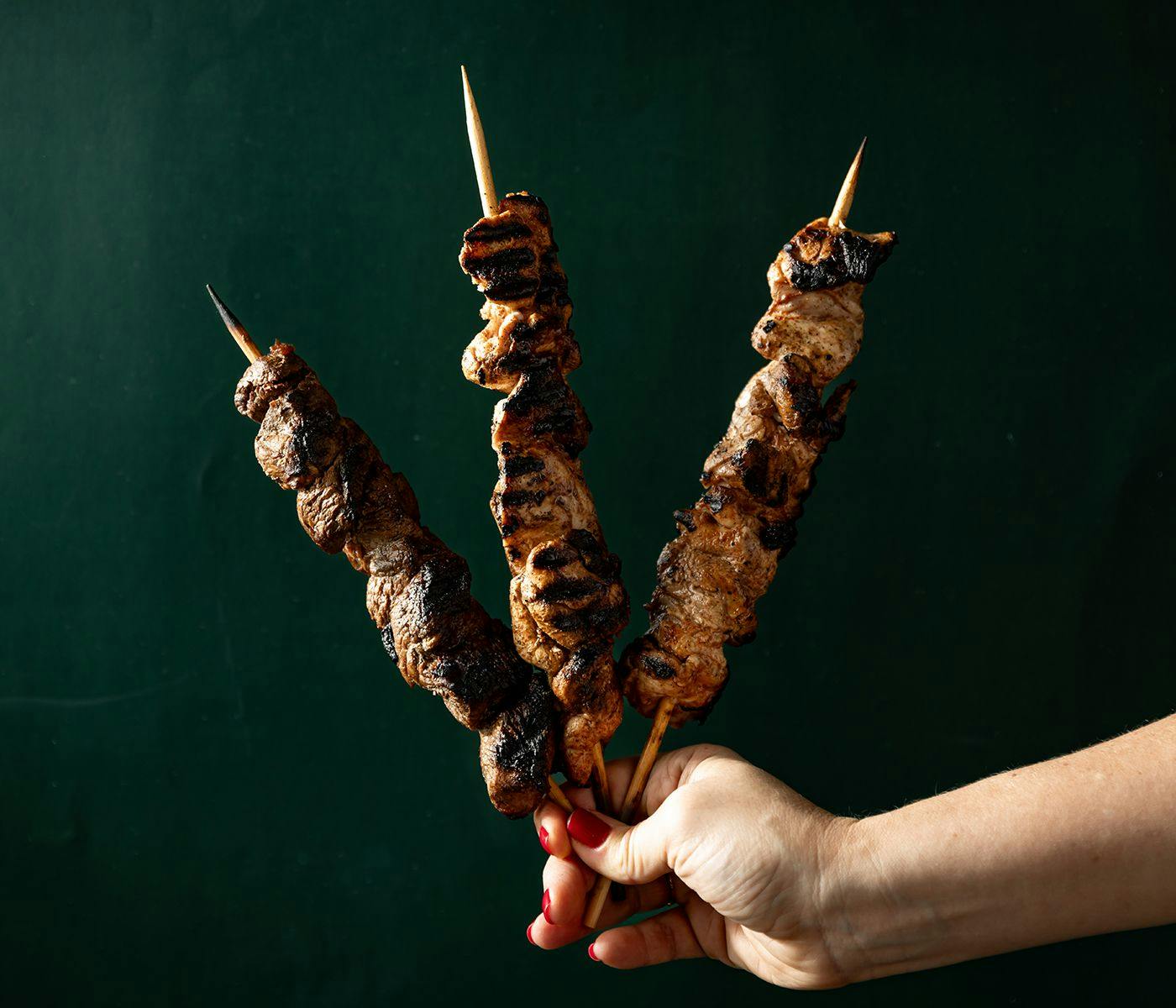 A hand holds 3 charred kebabs.