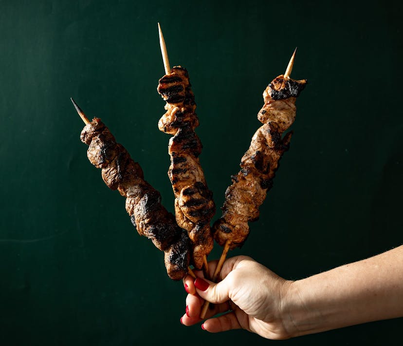 A hand holds 3 charred kebabs.