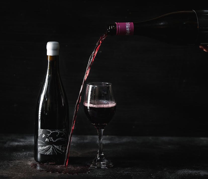 A bottle of red wine is poured towards a glass, missing - wine spilling over a black surface.