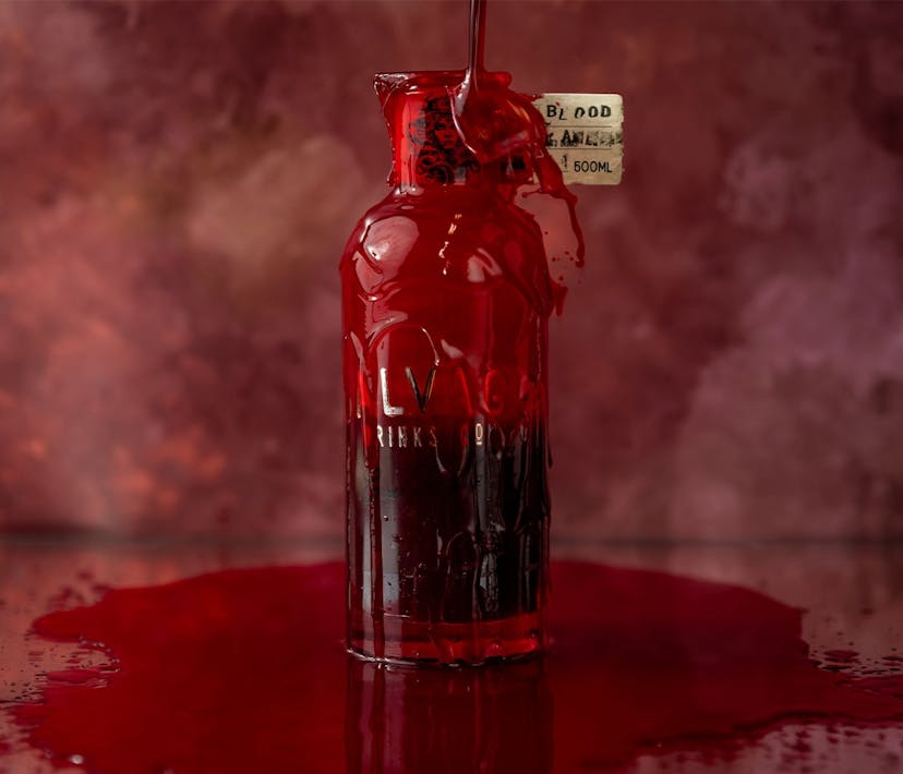 A bottle of dark red vodka, its contents spilled around its base.