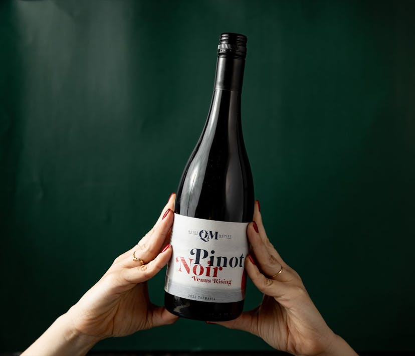 A bottle of Quiet Mutiny pinot noir held up with two hands.
