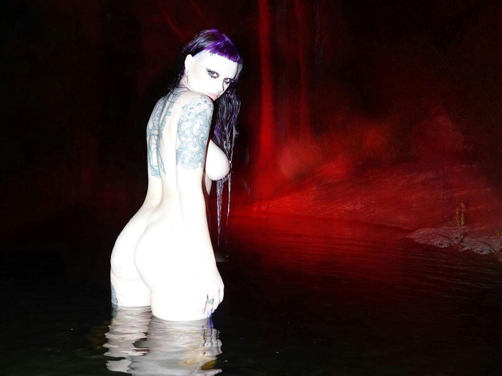Zheani stands naked, turned side on towards the camera, in a leg high pool of water.