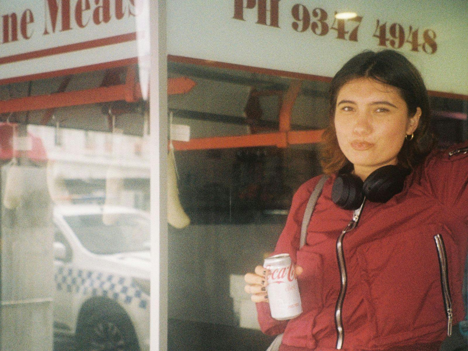 Kalyani wearing a red jacket, holding a Coca Cola in their hand.