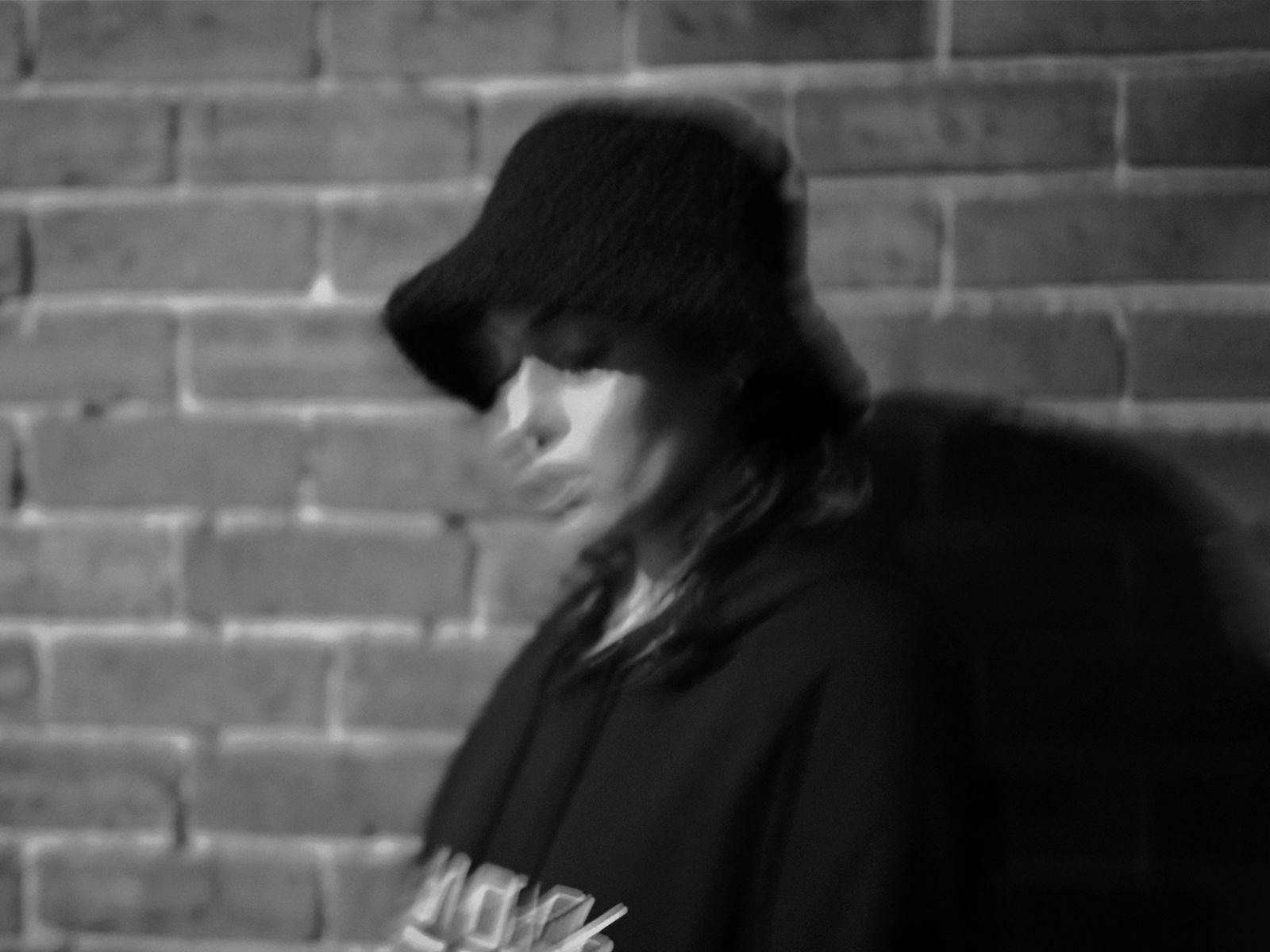A blurred black and white image of SOVBLKPSSY wearing a hoodie and bucket hat.