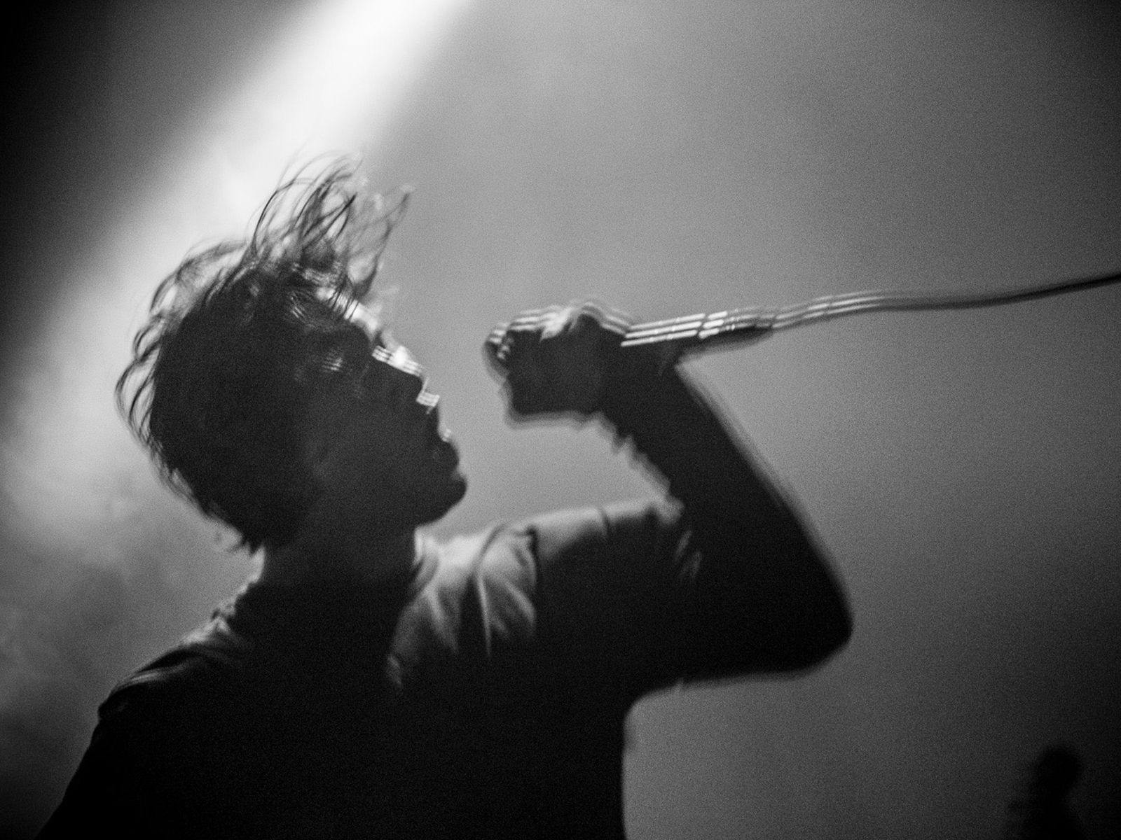 Buzz Kull performing with a microphone, their hair floating above them as they move their head.