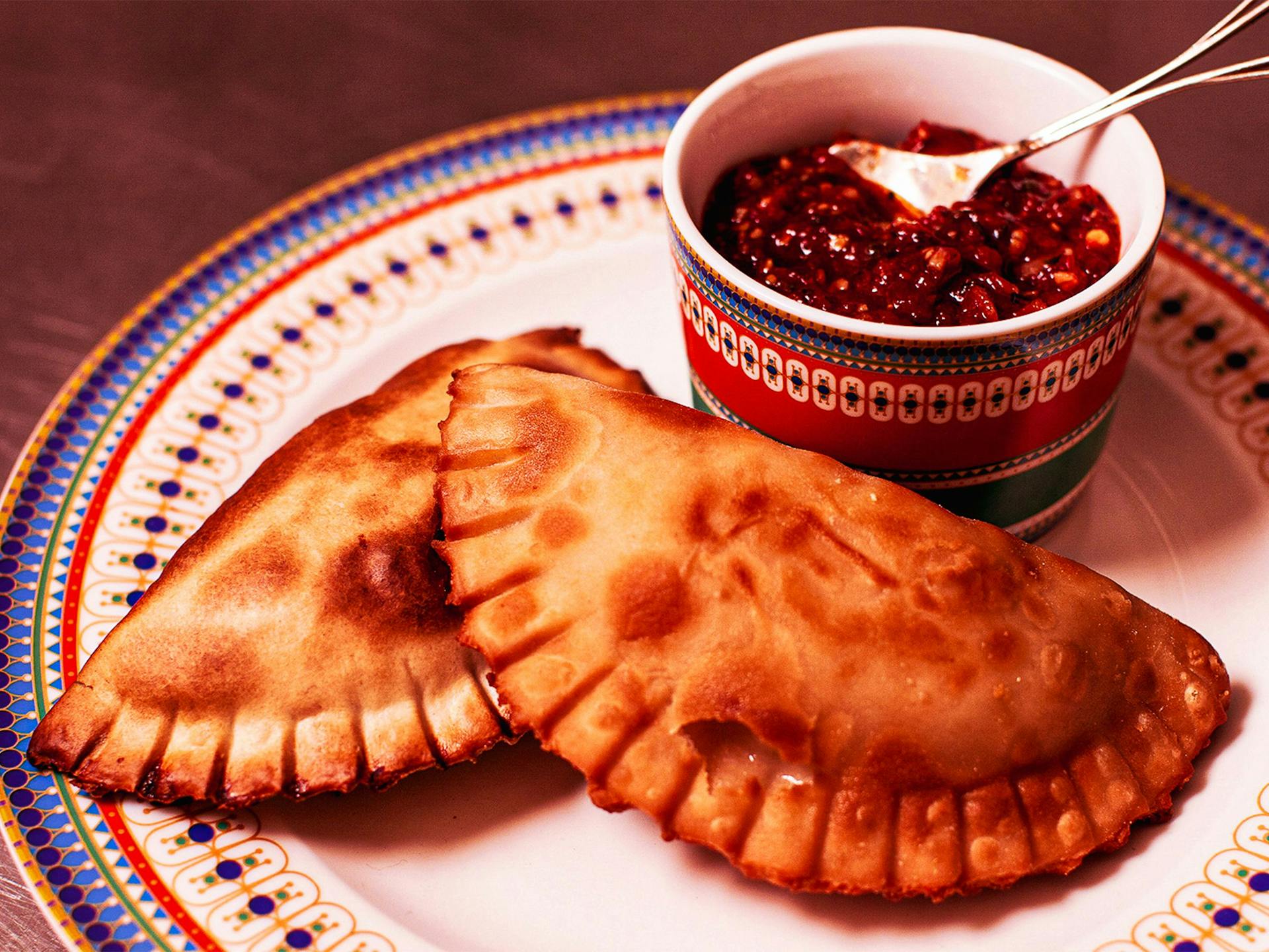 Two empanadas on a plate with a dipping sauce