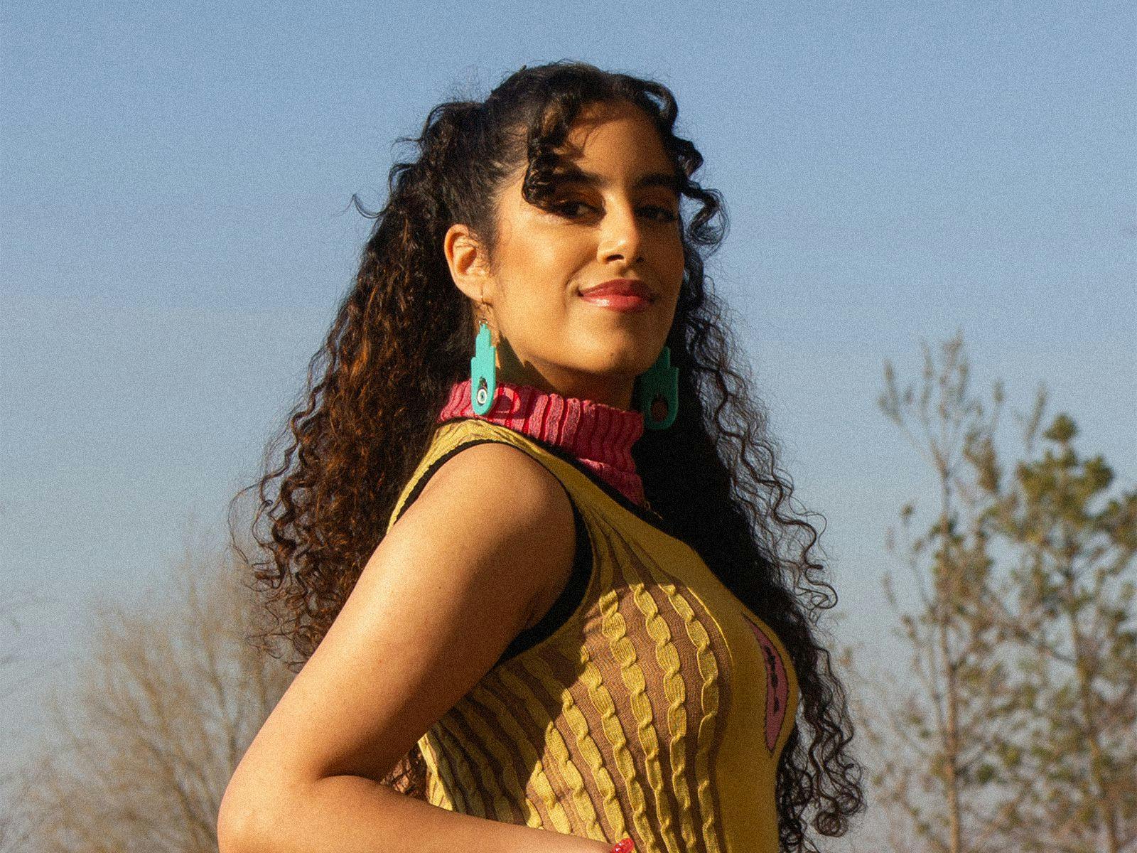 Nooriyah posing wearing a yellow top and big blue earrings.