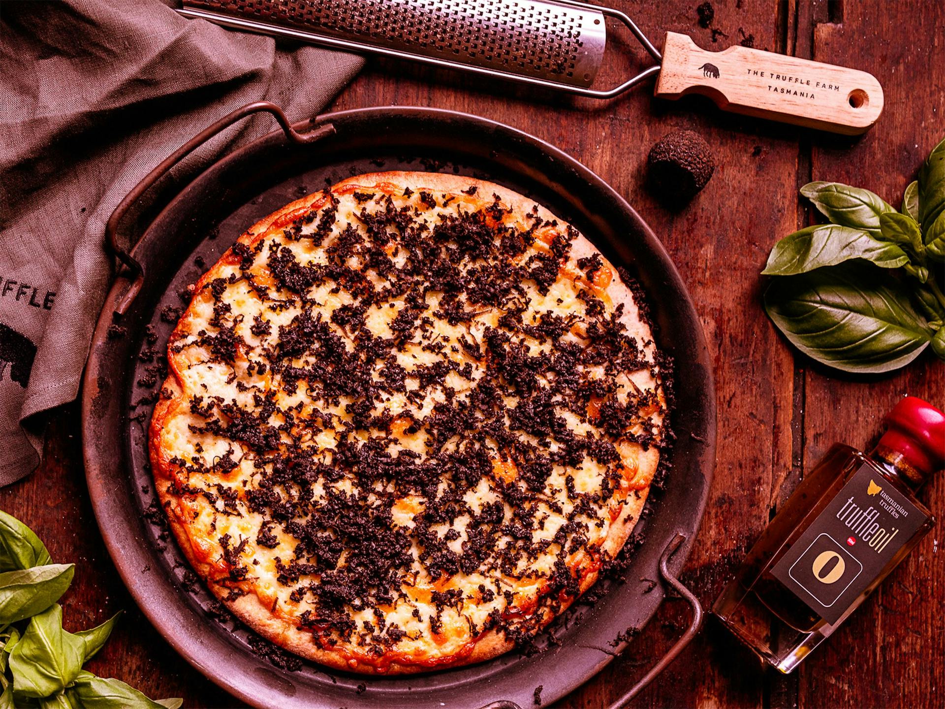 A truffle pizza sitting on a wooden table surrounded by truffle oil and basil