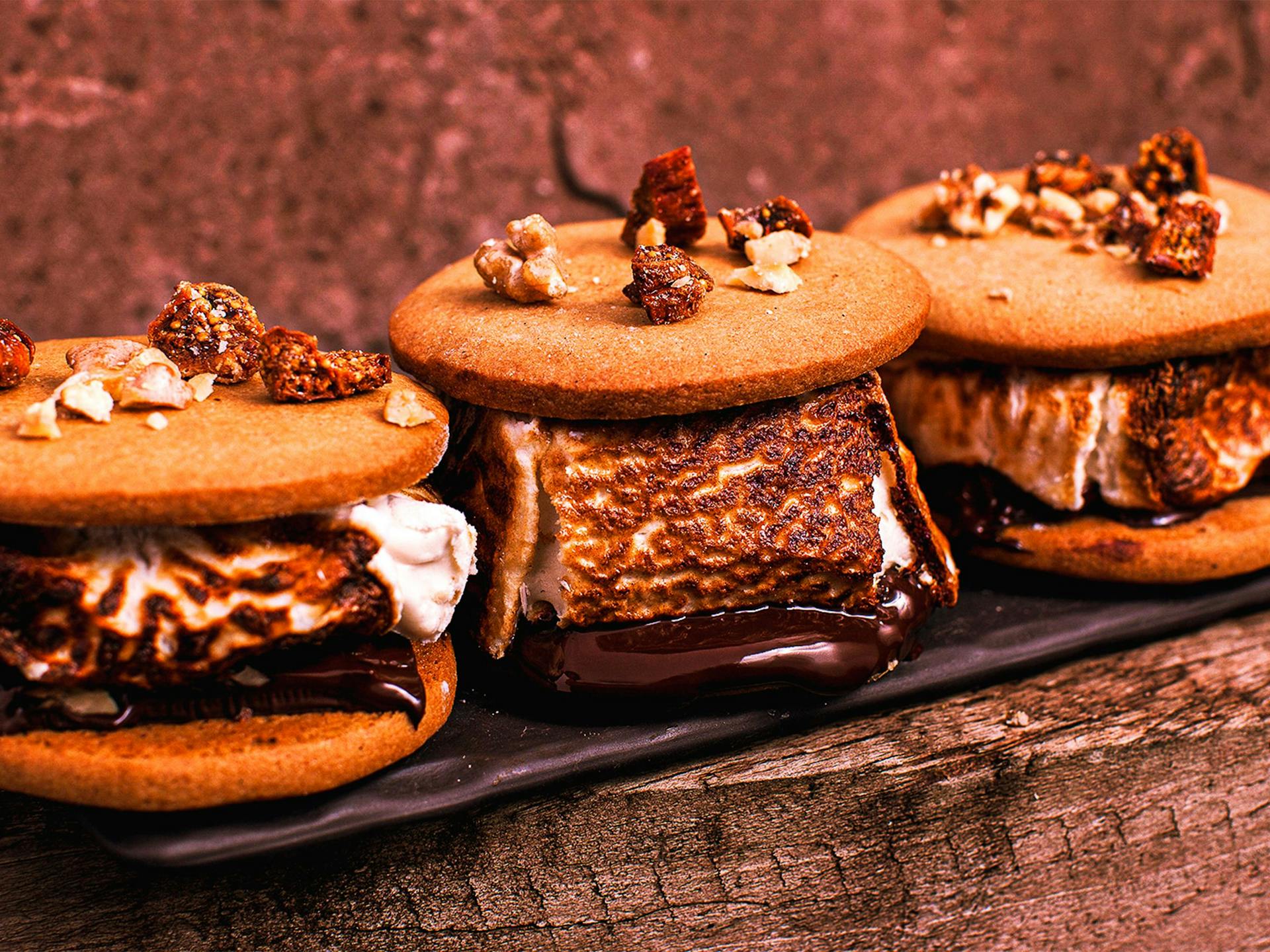 Three big smores overflowing with marshmallow sit atop a wooden log