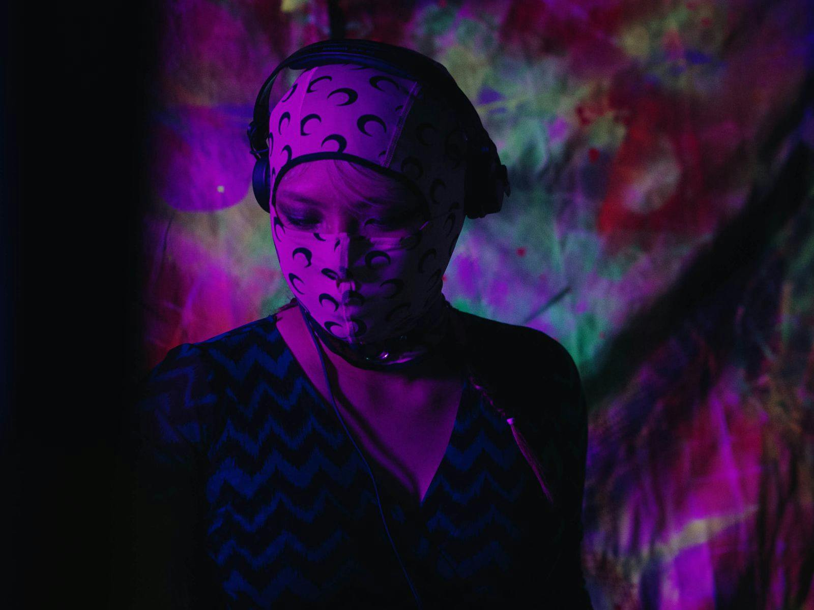 L$F in a dark, purple lit room wearing a hooded face covering.