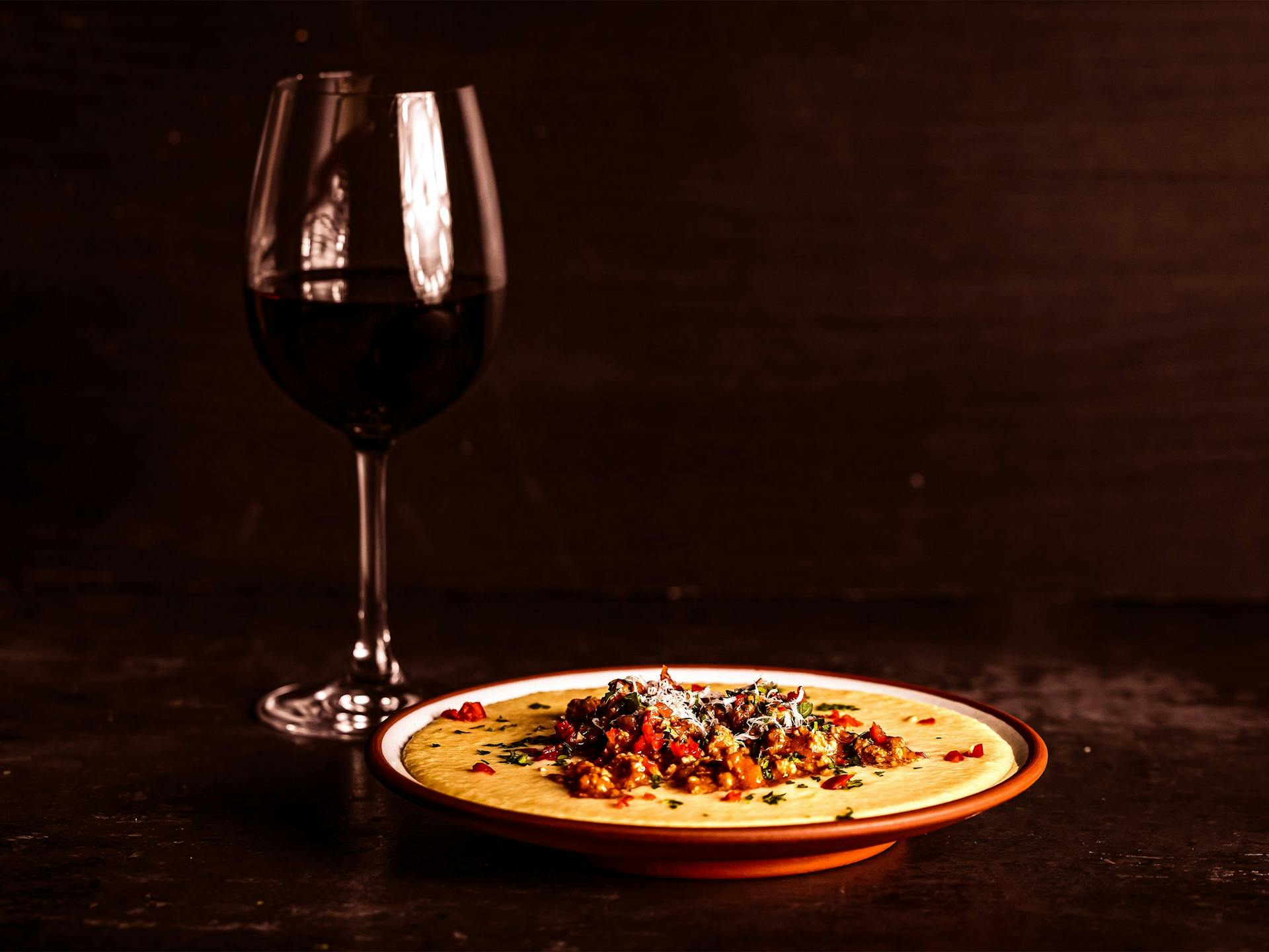 A glass of wine sits next to a bowl of creamy polenta