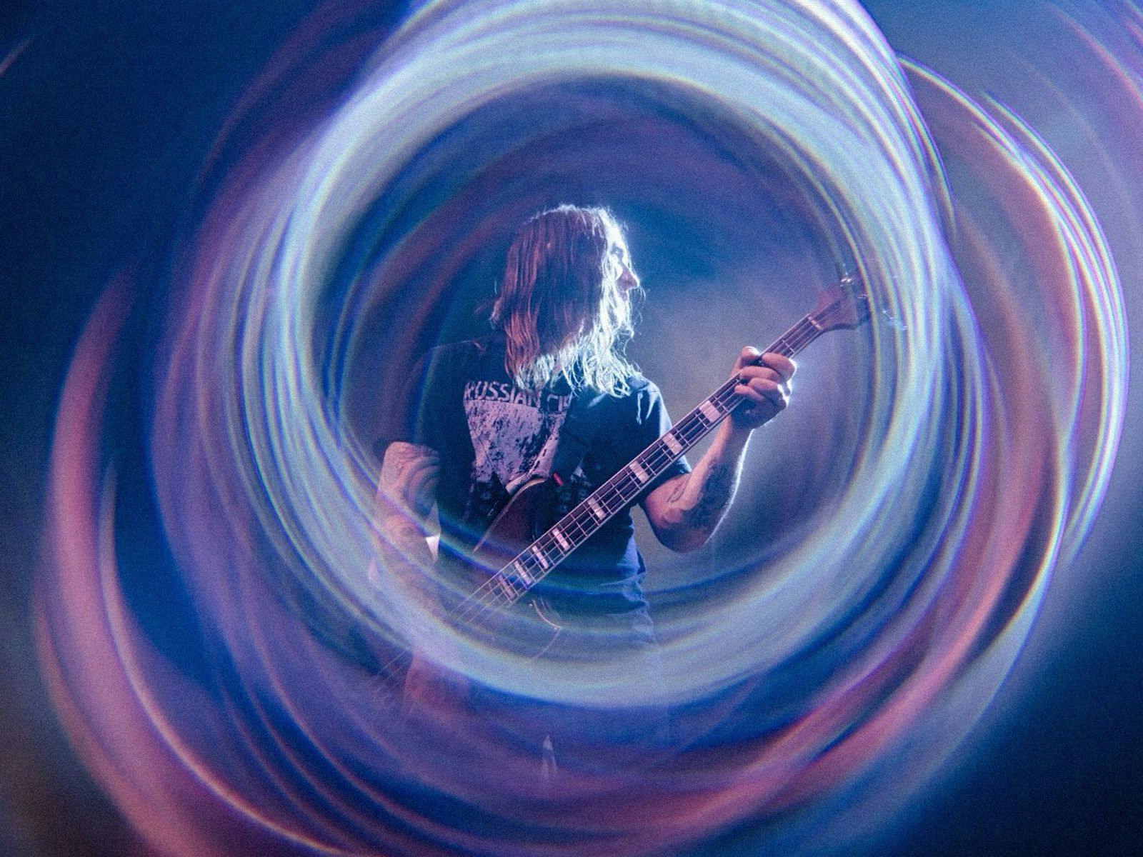 A guitarist on-stage, a long exposure photo gives the effect of circular lines of light around him.