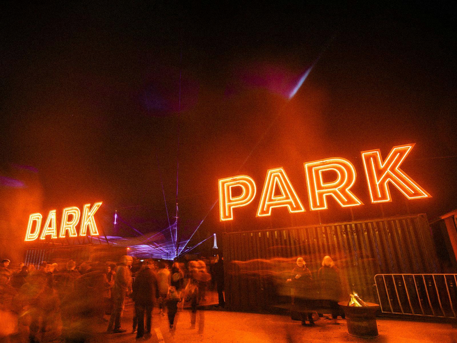 Massive neon letters spell out Dark Park, behind them a blue laser art exhibition.