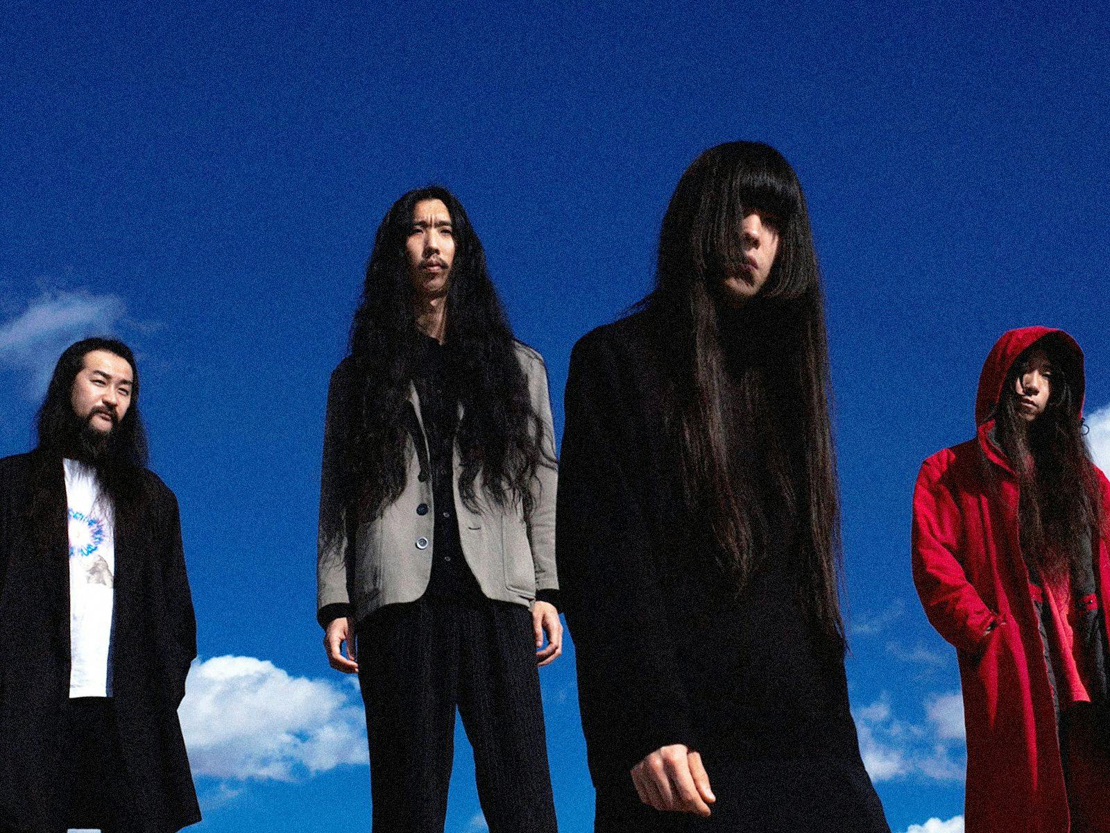 Four members of Bo Ningen pose, a lightly clouded blue sky their backdrop.