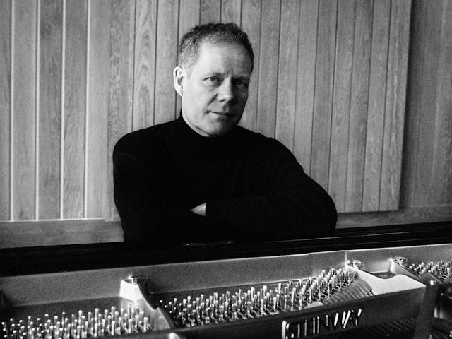 Max Richter poses seated, leaning on his piano.