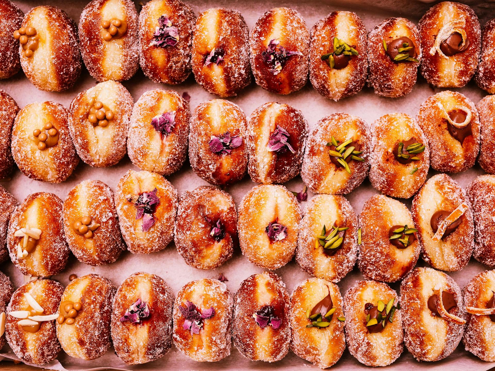 Dozens of donuts lie face up with jam and other fillings on display 