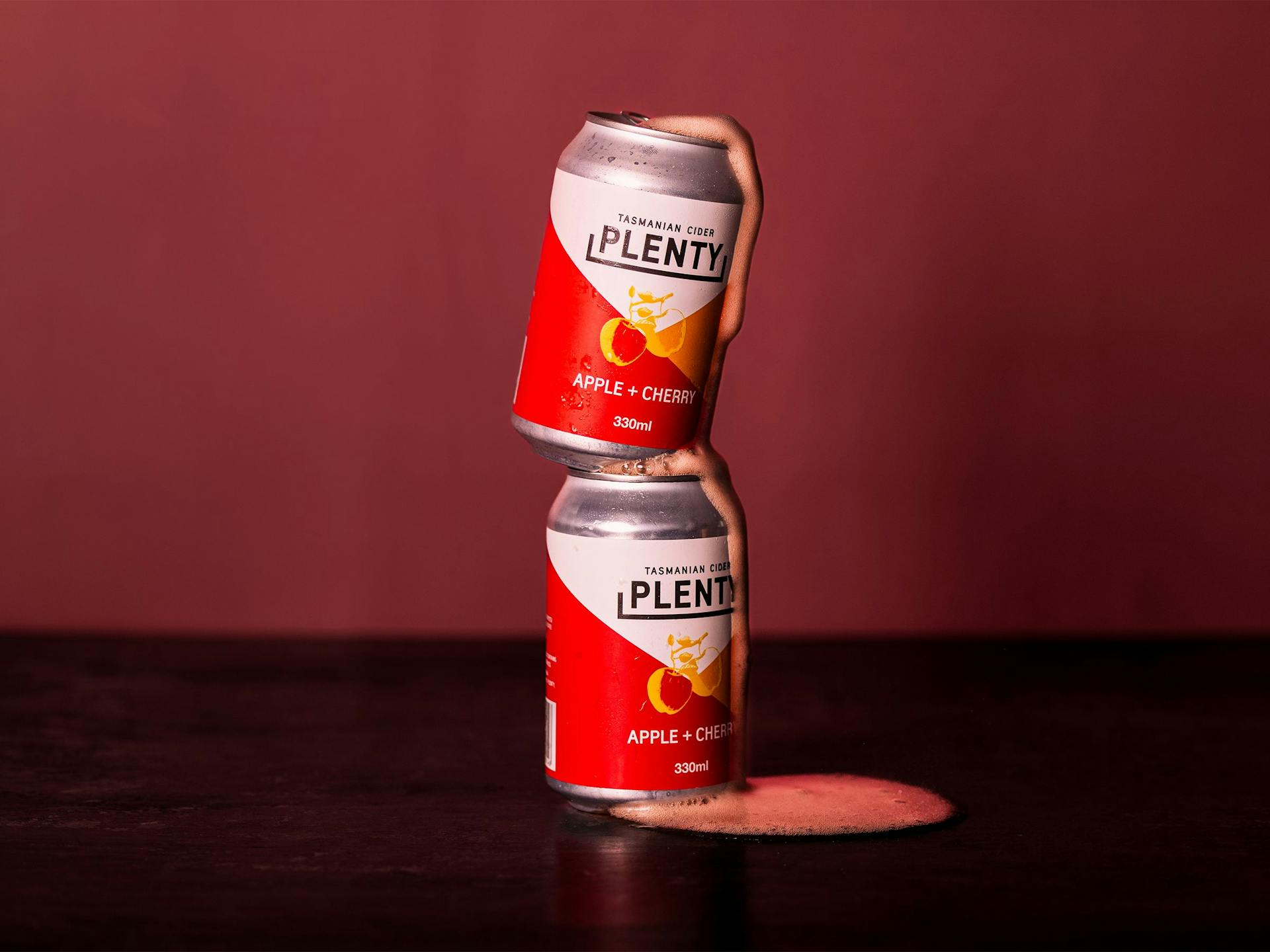 Two cans of Plenty Cider balance atop each other, overflowing with foam