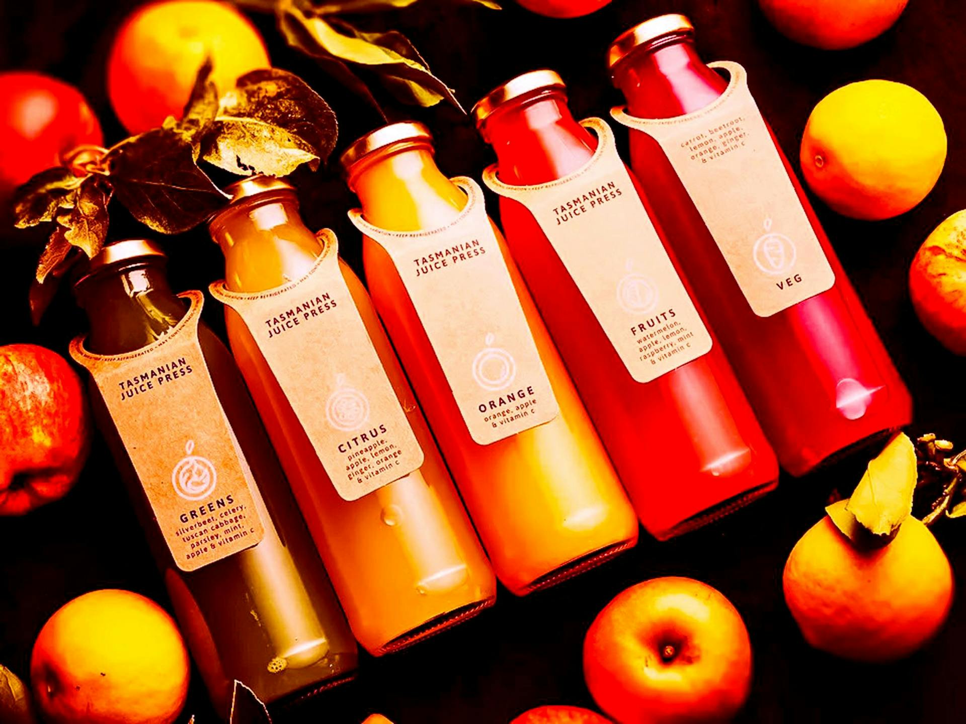A lineup of cold pressed juices surrounded by fruit