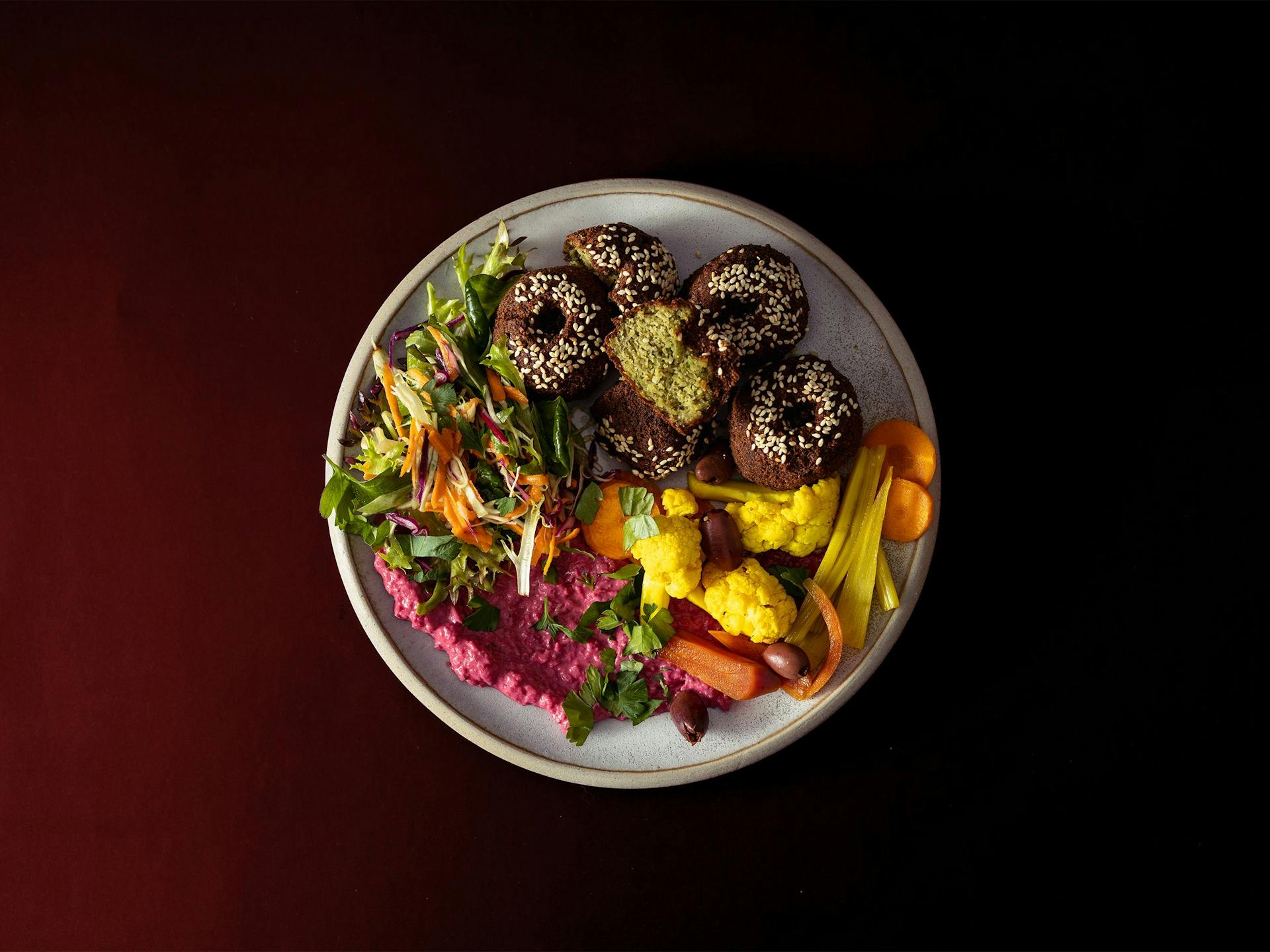 A brightly coloured falafel plate with beetroot hummus and pickled vegetables
