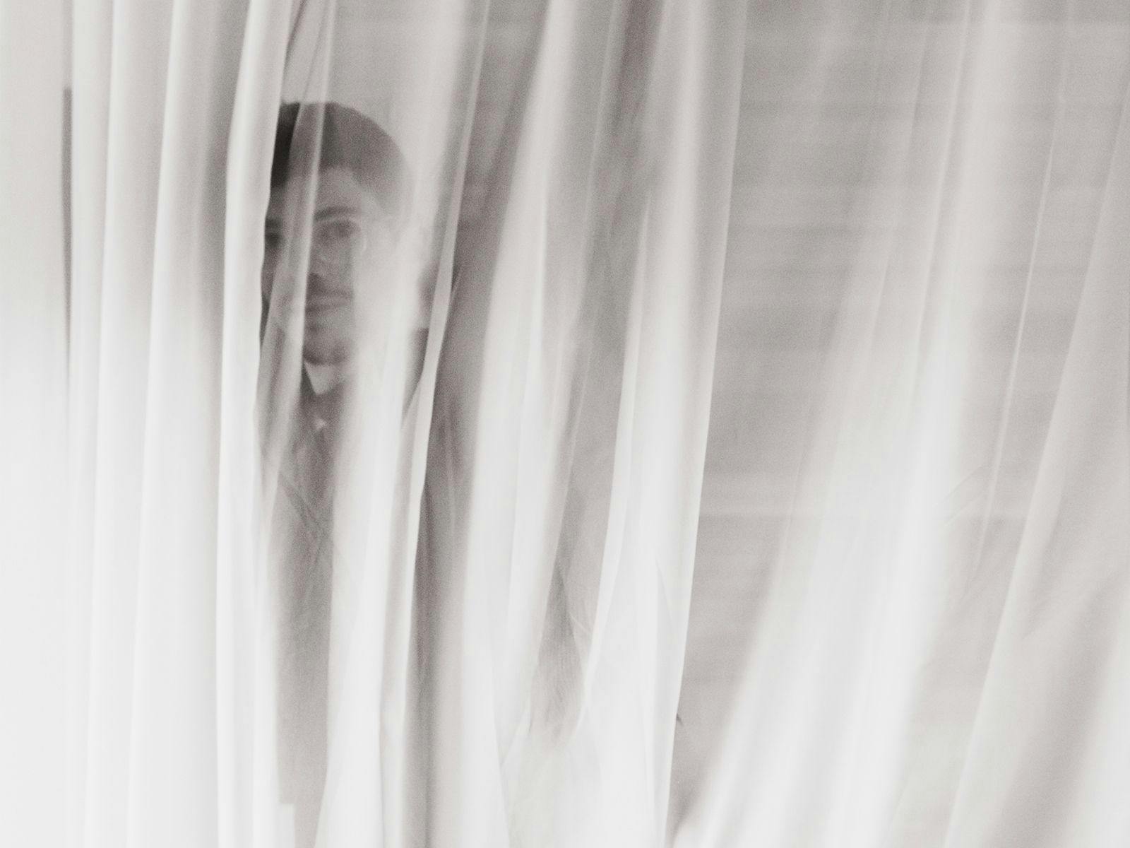 Fabian B hides behind a semi-opaque curtain.