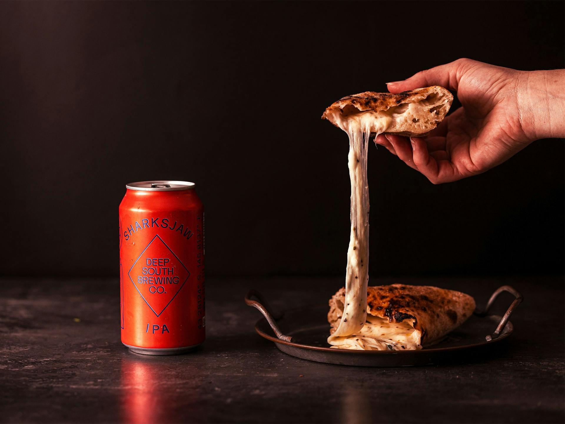 A pizza pocket oozing with cheese sits next to a can of beer