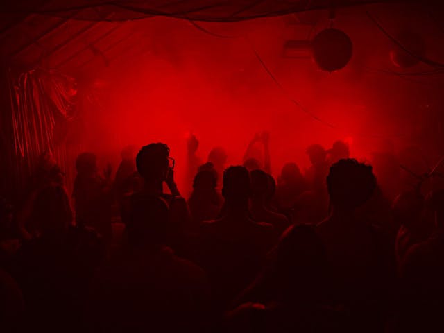Several people facing towards a DJ setup. Red lights fill the room.