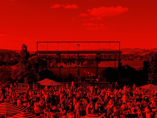 A red-washed image of hundreds of people relaxing, drinking and listening to music on the lawns at Mona.