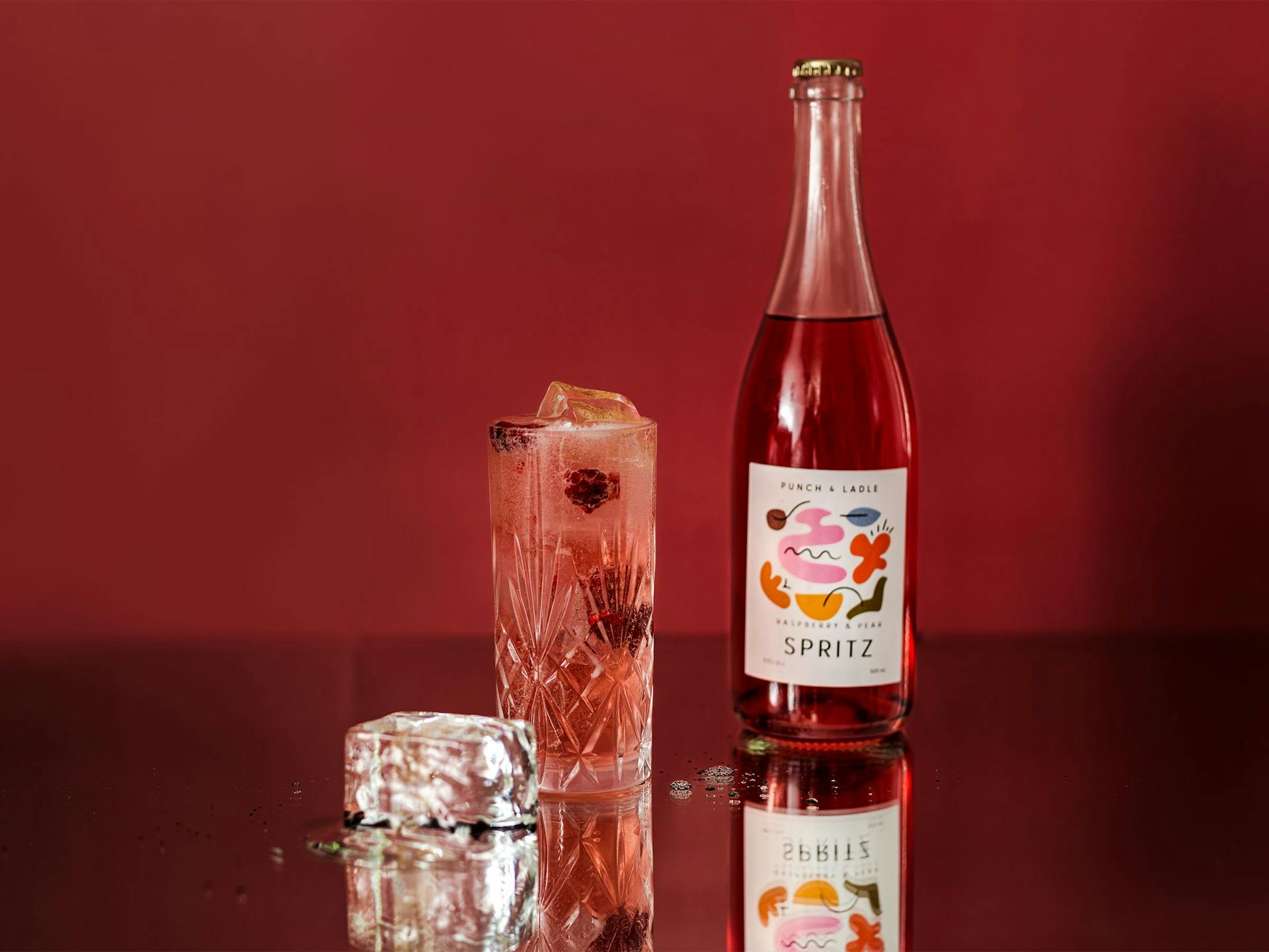 A Punch & Ladle bottle sitting next to a tall Spritz with raspberries and ice