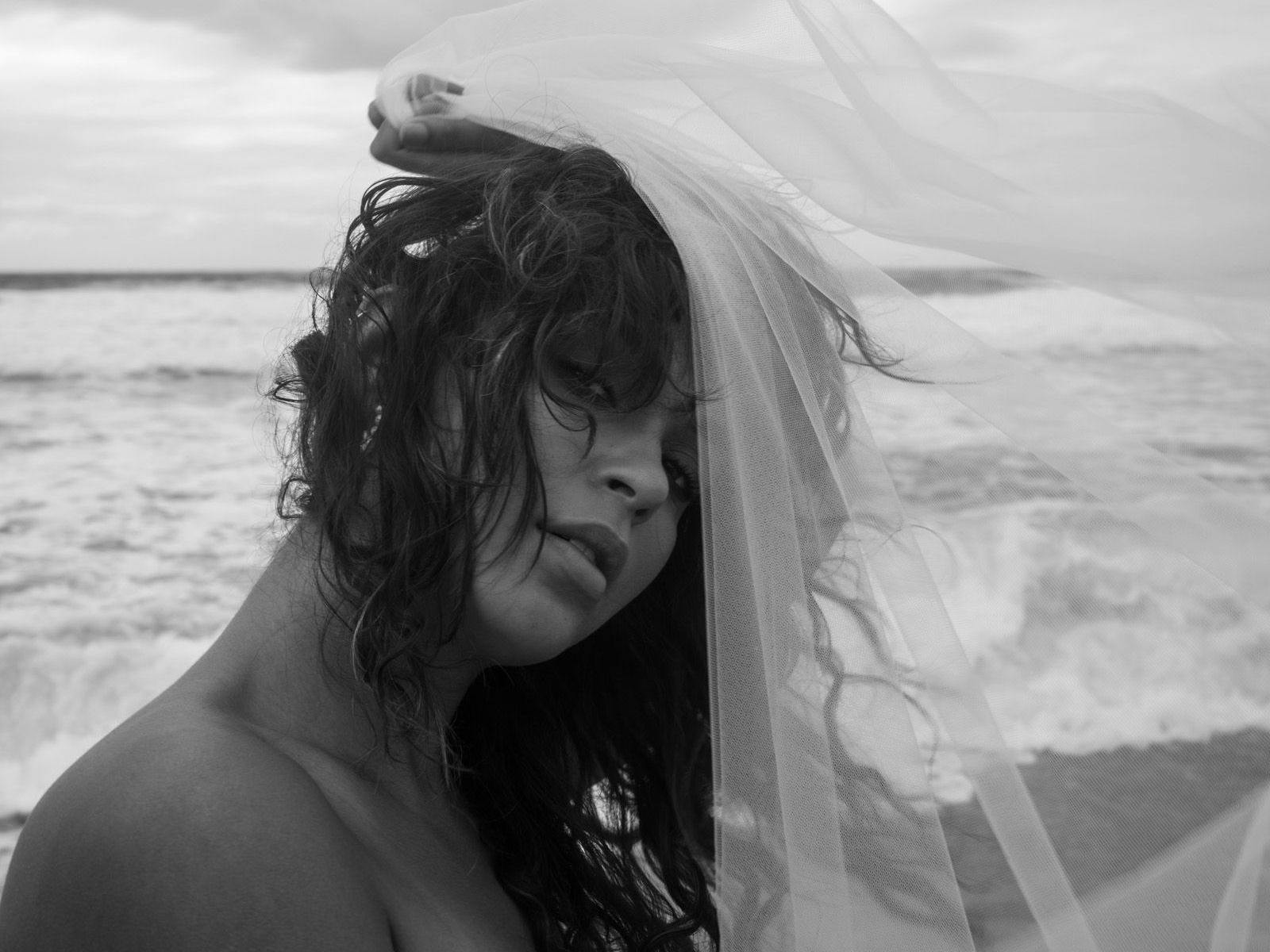 Claire O'Brien at a beach, holding a veil-like piece of material across their head.