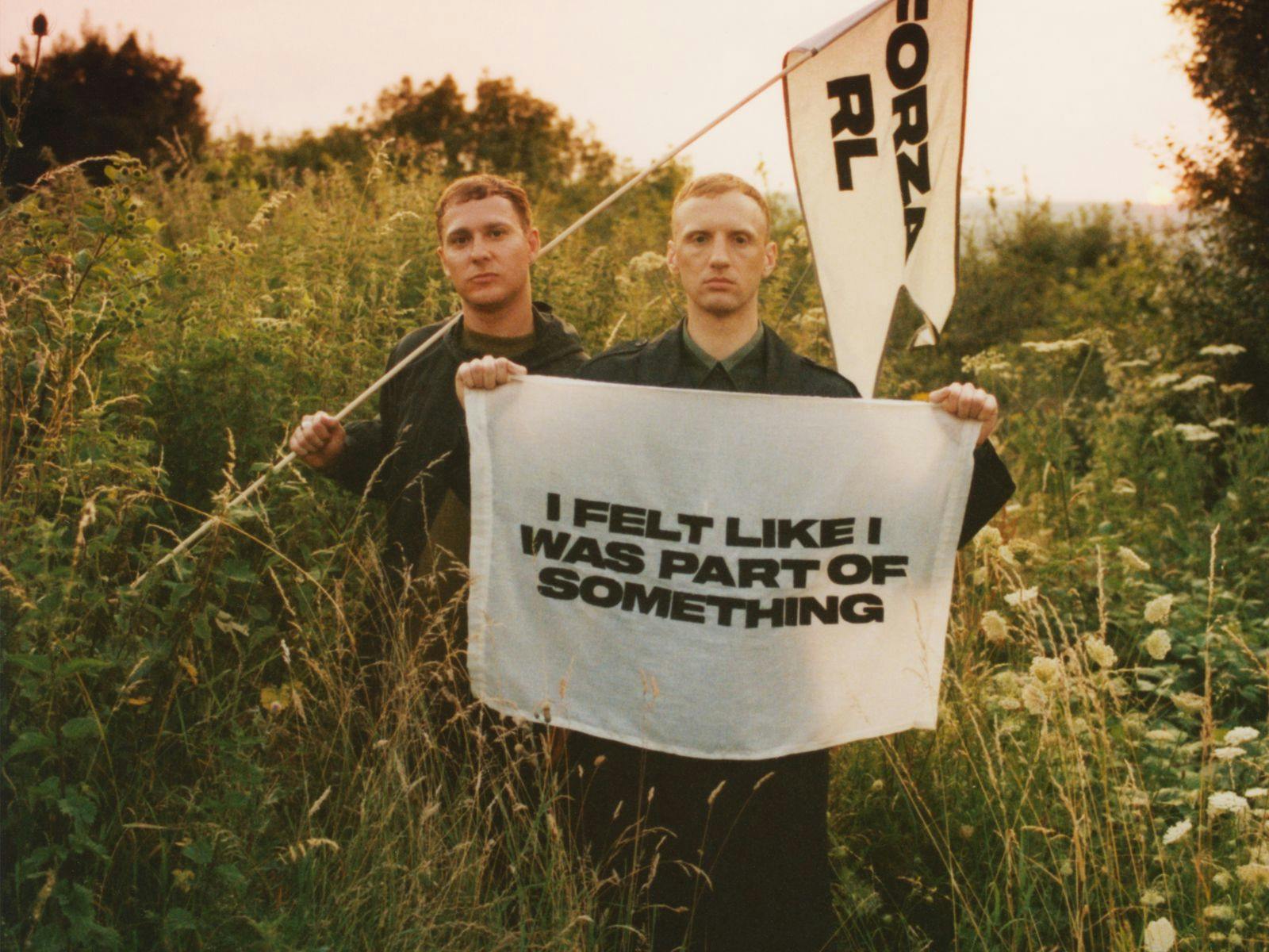 Real Lies holding up a cloth sign that reads "I felt like I was part of something"