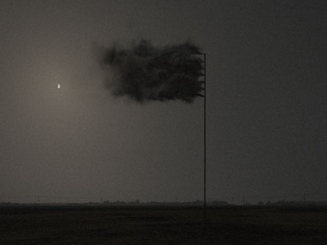 A black flag made up entirely of billowing smoke against a night sky background.