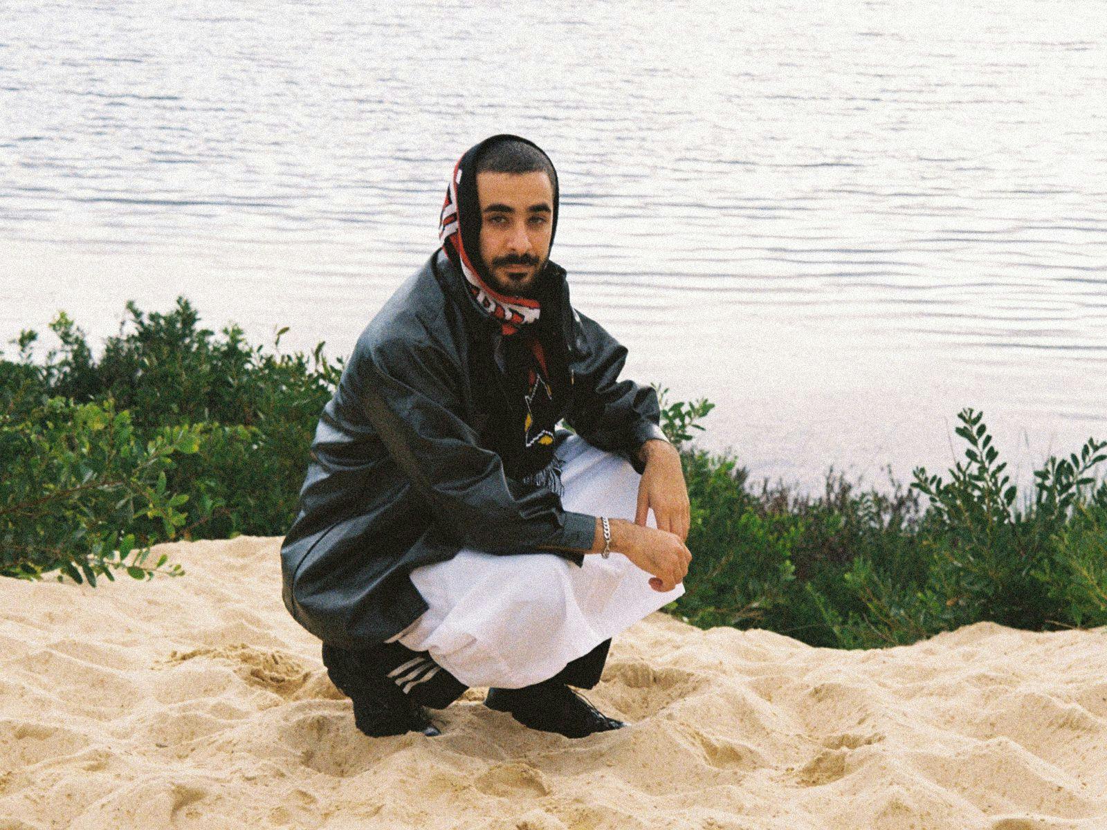 Moktar crouched on the ground at a beach.