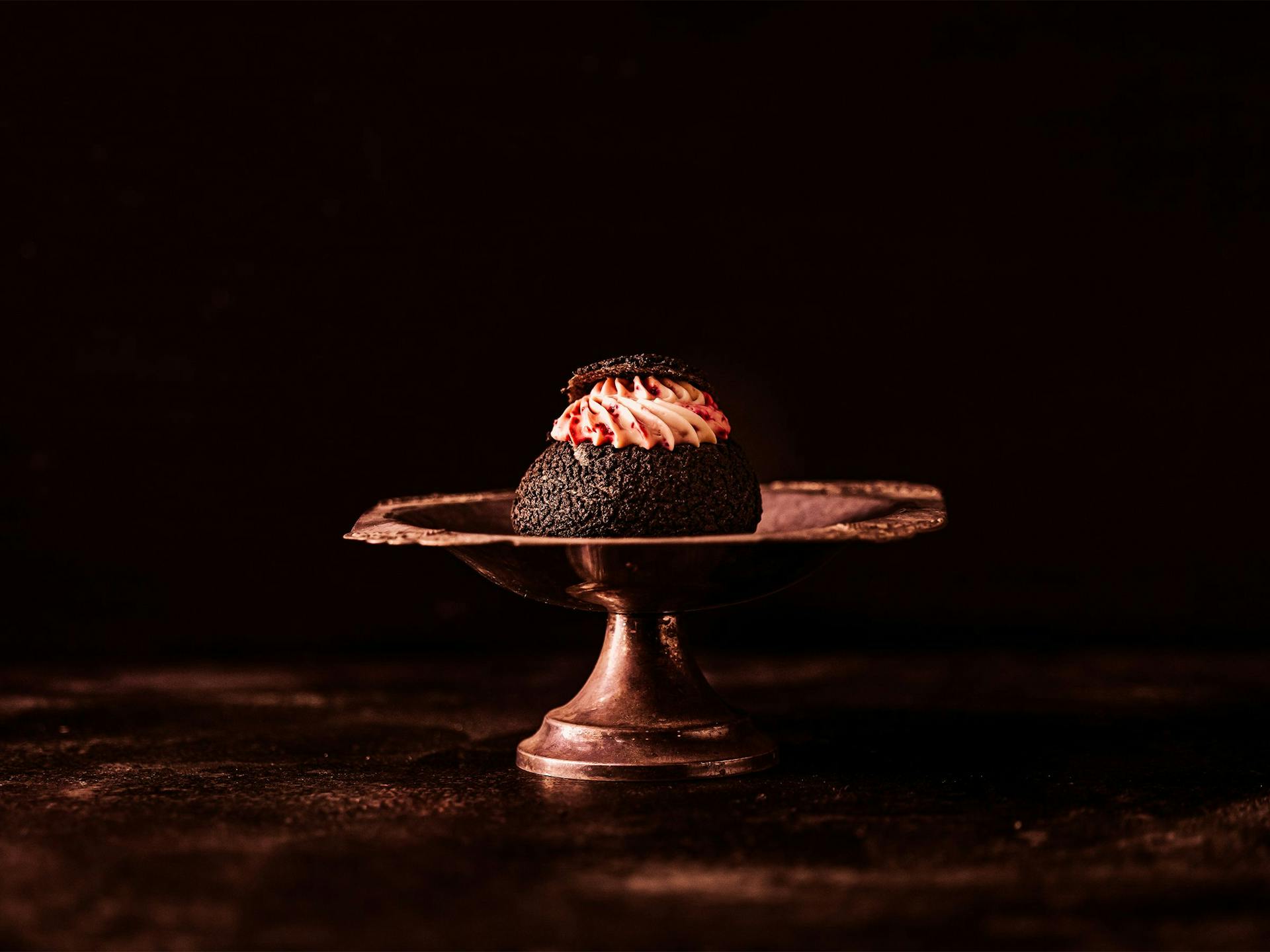 A dark chocolate woofee pie sits atop an elegant metal cake stand