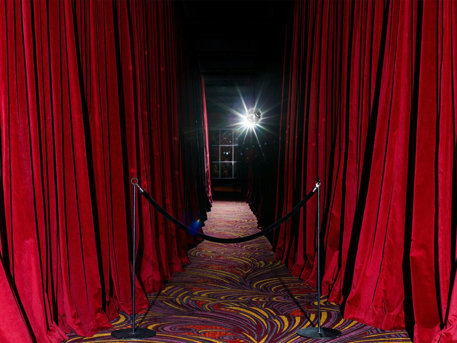 A creepy carpeted hallway, lined by long red velvet curtains.