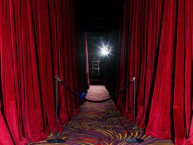 A creepy carpeted hallway, lined by long red velvet curtains.