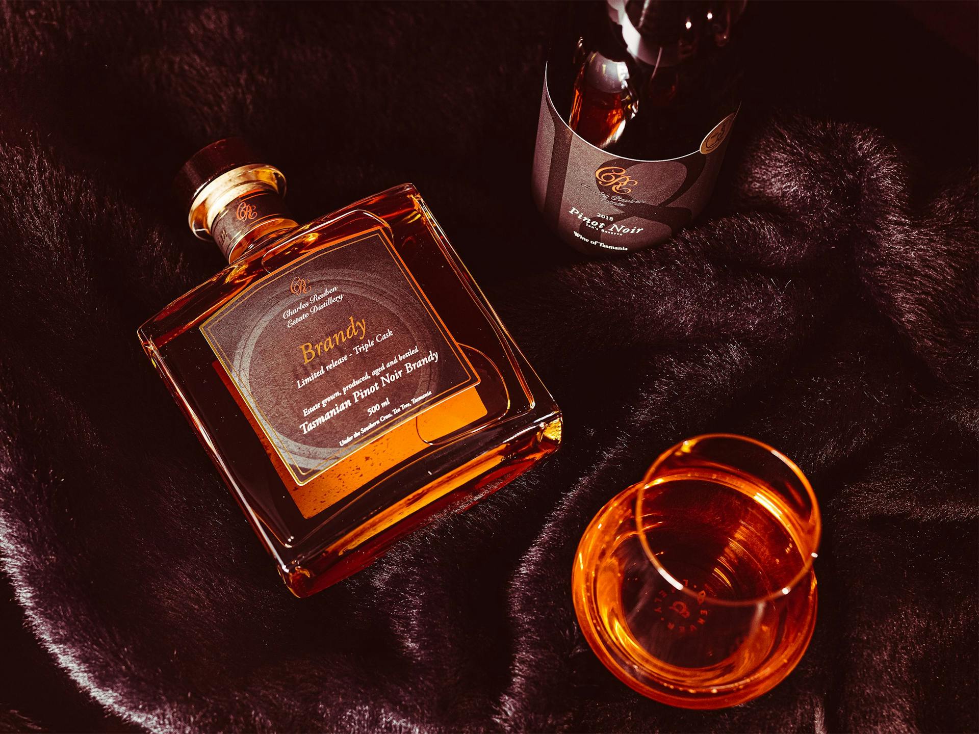 A bottle of brandy and pinot noir sit on black faux fur