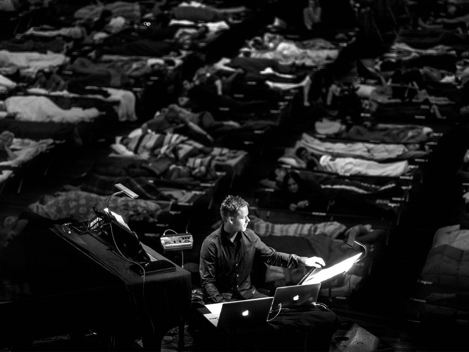 Max Richter performing, with several people sleeping in beds behind him.
