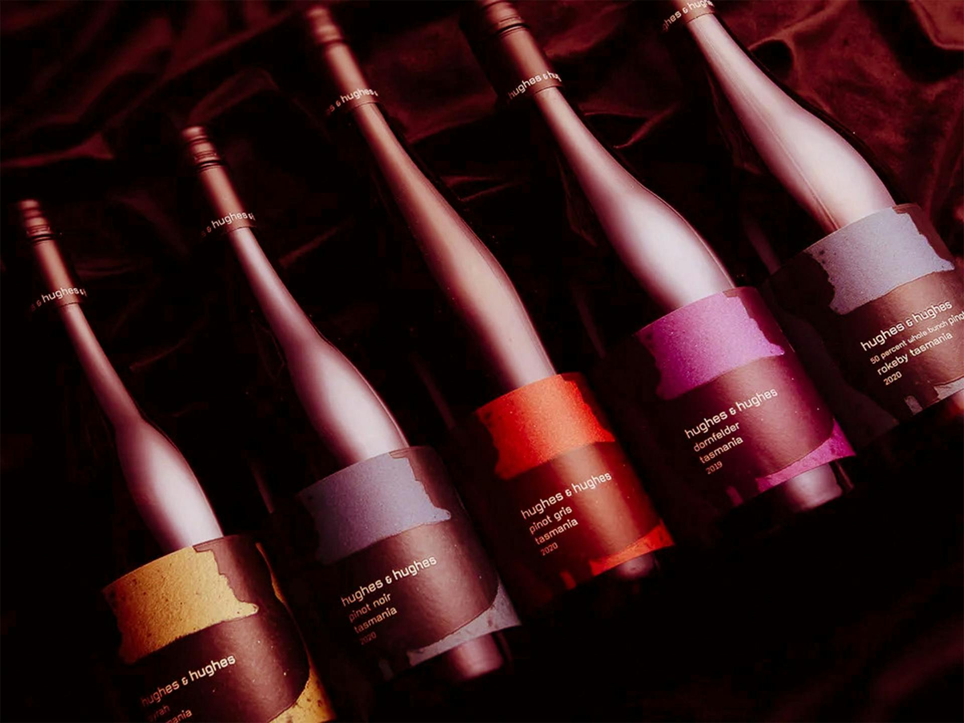 Five bottles of wine with different colour labels laid down on red velvet
