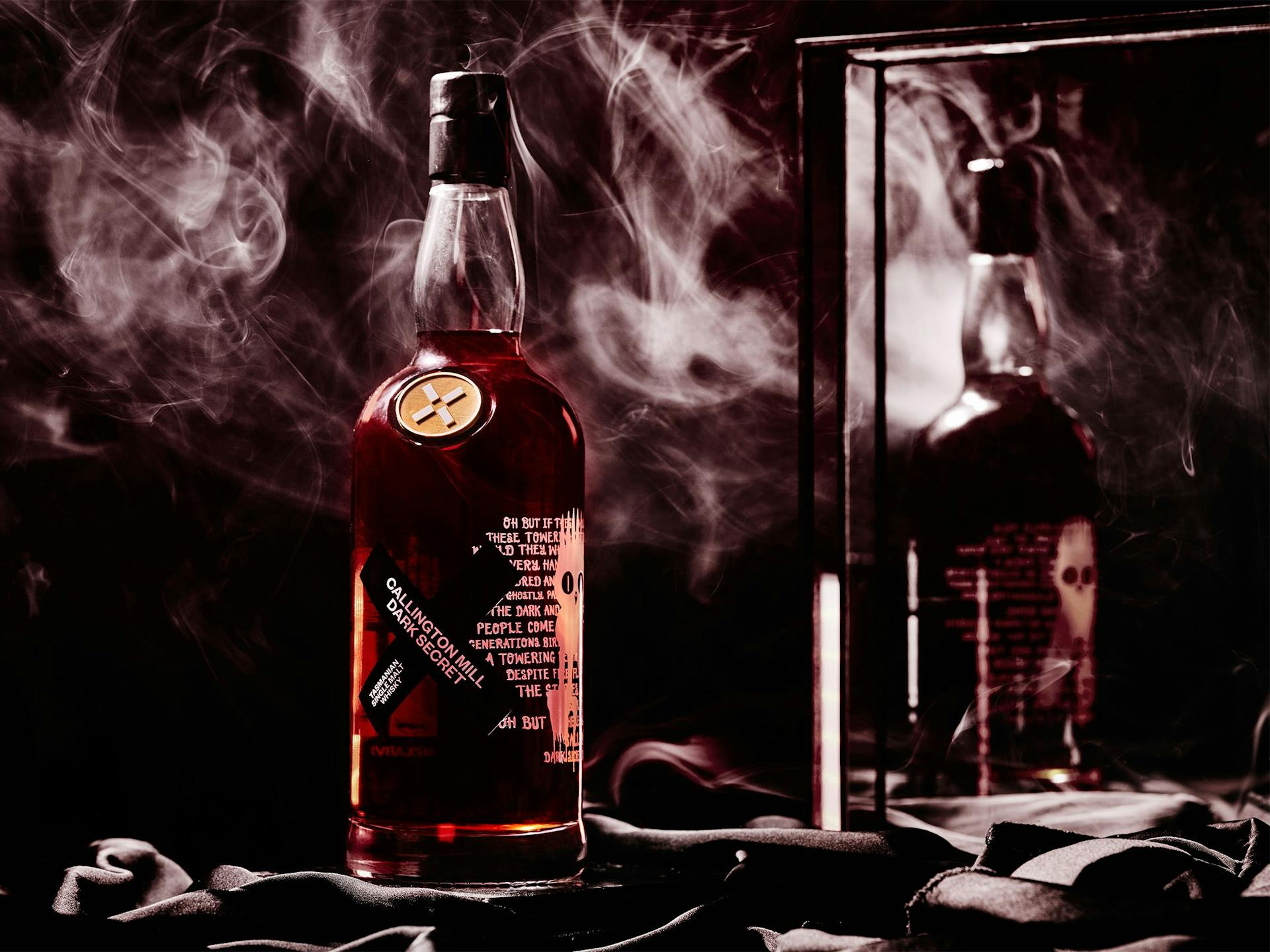 A bottle of Callington Dark Secret reflected in a mirror and surrounded by smoke