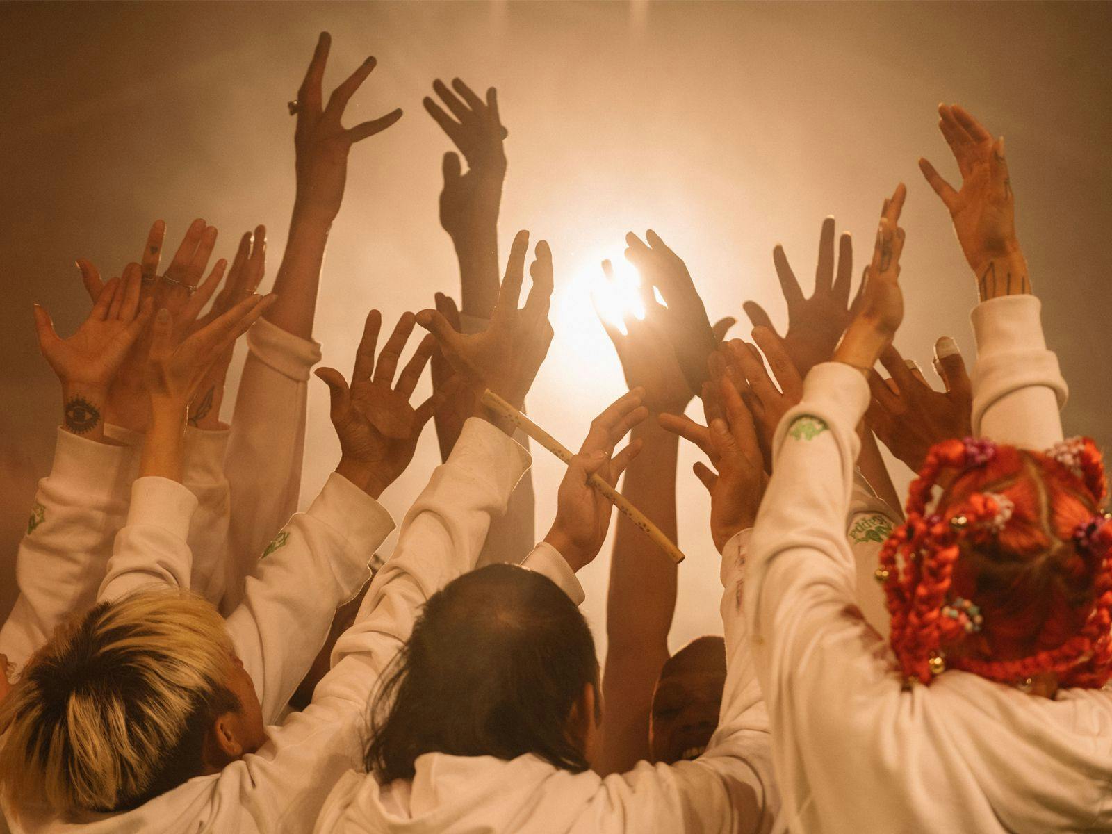 Several people hold their arms in the air up to a bright yellow light.
